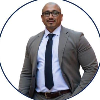 Steven Ramirez, in glasses, a grey suit and navy tie, against a white background